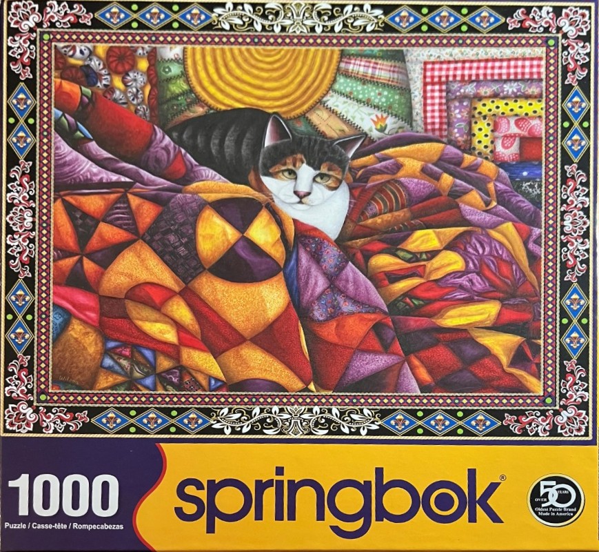 A tricolor cat resting on a colorful geometric patchwork quilt inside an ornate decorative border.