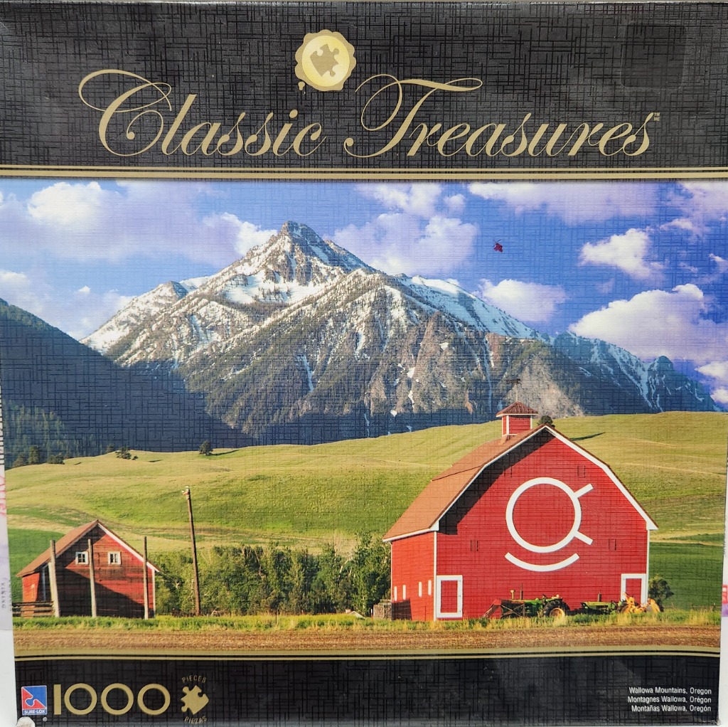A red barn in a field with snow-capped Wallowa Mountains in the background.