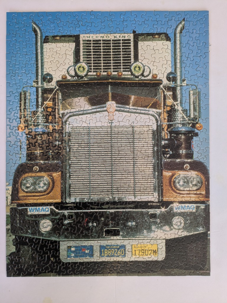 Front view of a semi-truck with a large chrome grille and two license plates.
