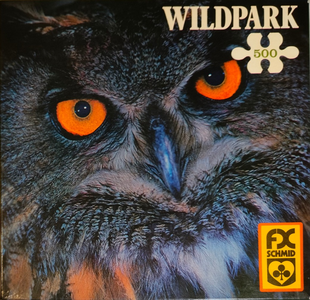 Close-up photographic portrait of an owl with piercing orange eyes and dark, textured feathers.