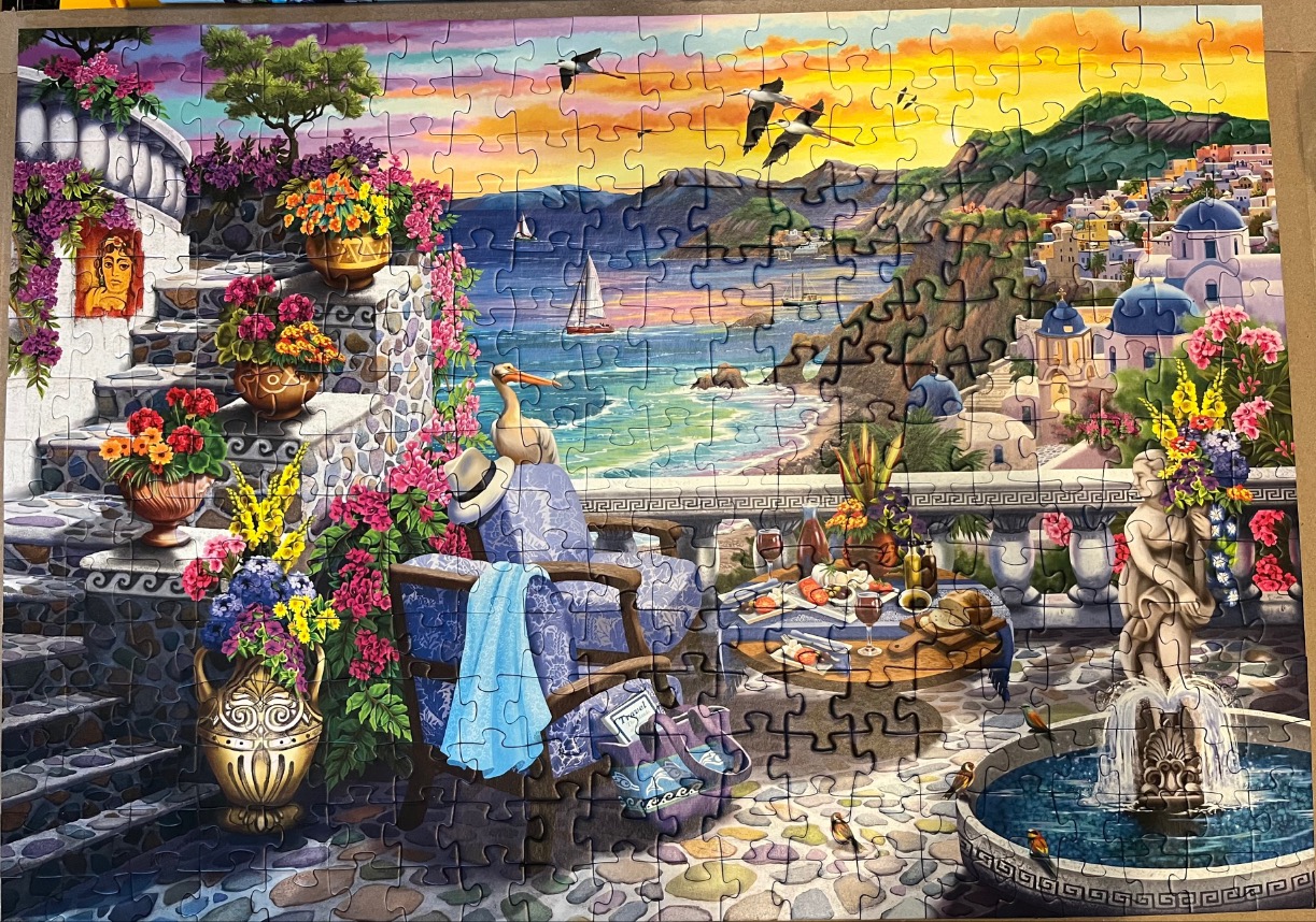 A Mediterranean terrace scene with flowers, a fountain, and a coastal view at sunset.