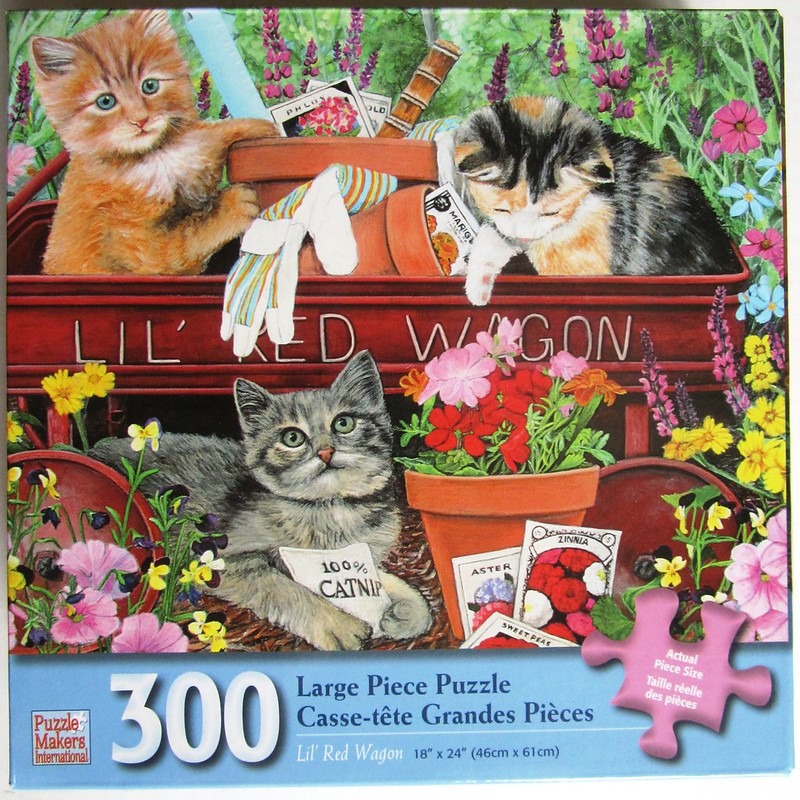Three kittens playing in and around a vintage red toy wagon filled with gardening supplies and flowers.
