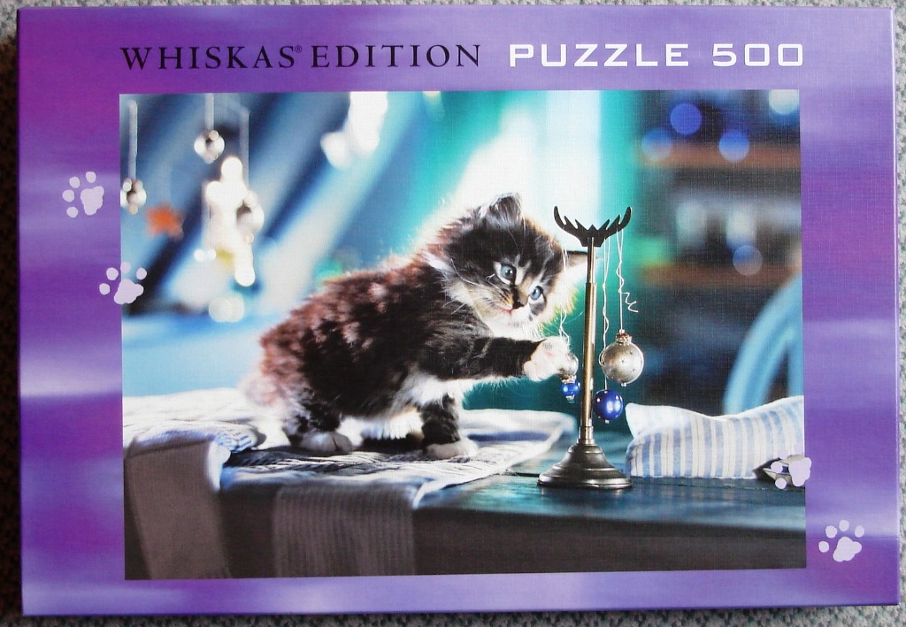 A fluffy black and white kitten playing with hanging blue and silver ornaments on a table.