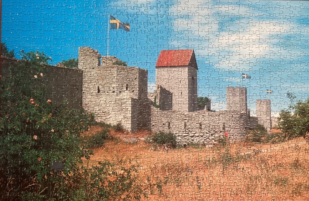 An ancient stone city wall with towers and Swedish flags flying under a blue sky.