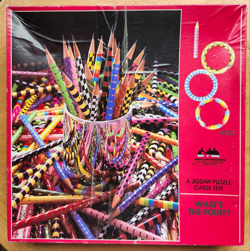 A metallic cup filled with colorful patterned pencils, surrounded by a chaotic pile of more pencils.