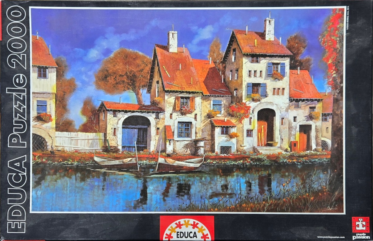 An oil painting of a rustic European waterside village with red-roofed cottages and two small wooden boats.