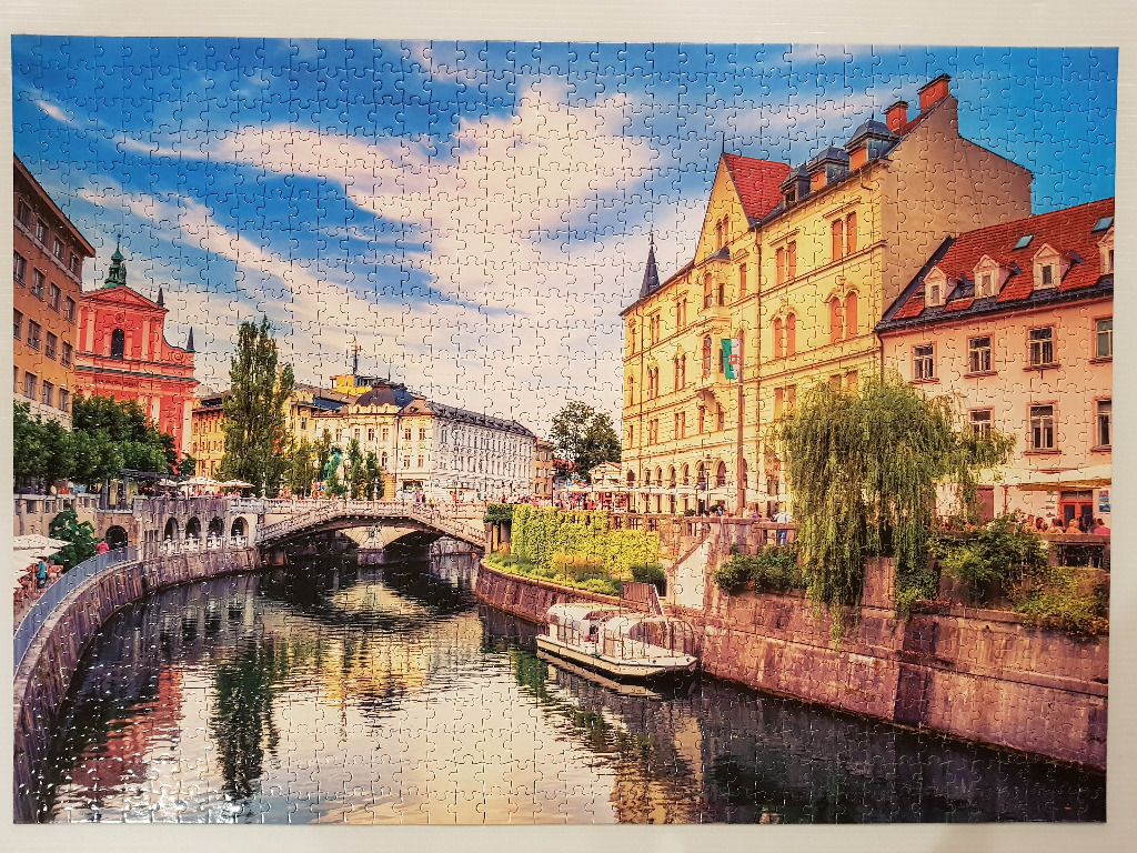A riverside view of Ljubljana, Slovenia, featuring the Triple Bridge and the pink Franciscan Church of the Annunciation.