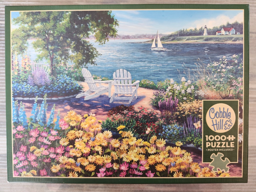 Two white Adirondack chairs overlooking a blue bay with a sailboat and a distant lighthouse.