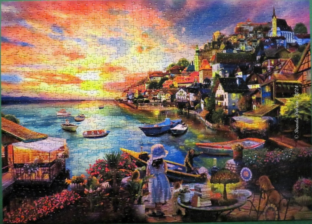 A vibrant sunset scene over a European hillside village and harbor.