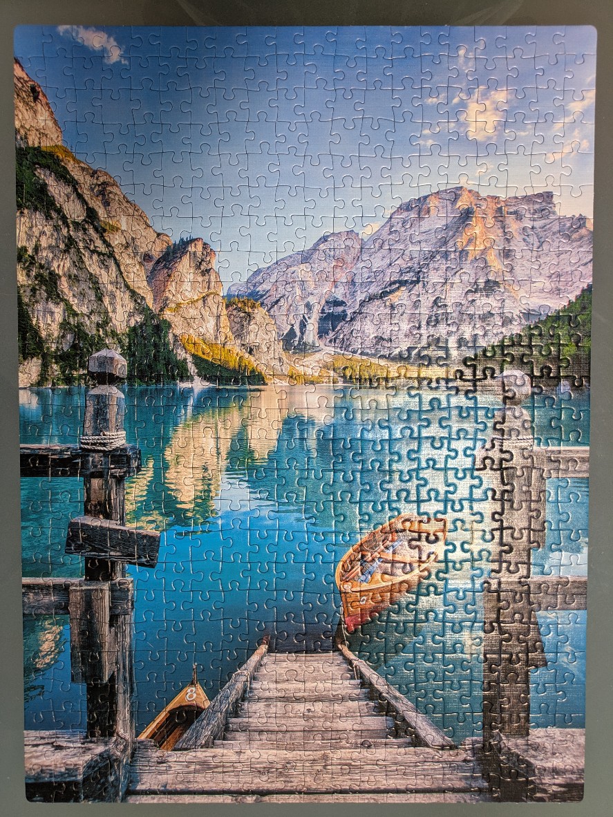 A peaceful mountain lake scene with a wooden pier, a small boat, and tall craggy cliffs under a clear blue sky.