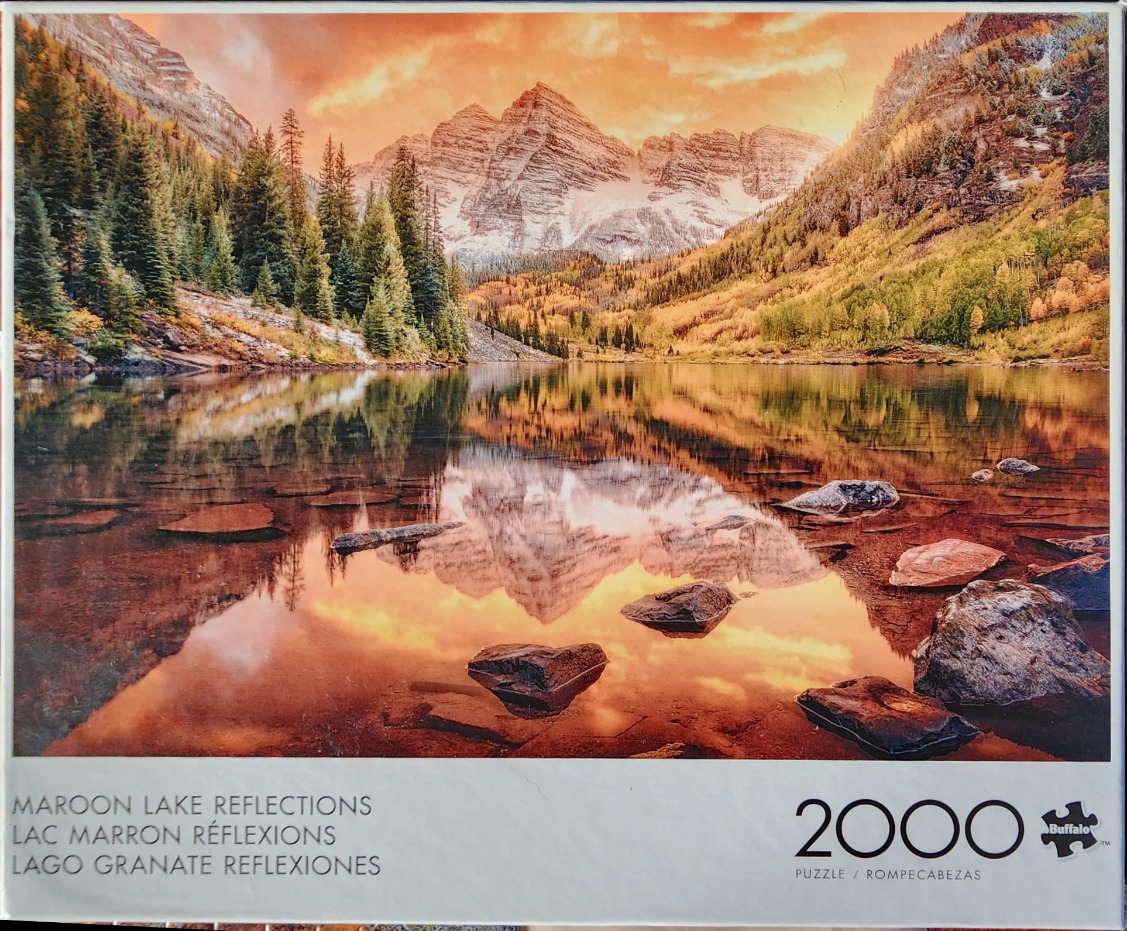 A scenic mountain landscape featuring the Maroon Bells reflected in a calm lake during autumn sunset.
