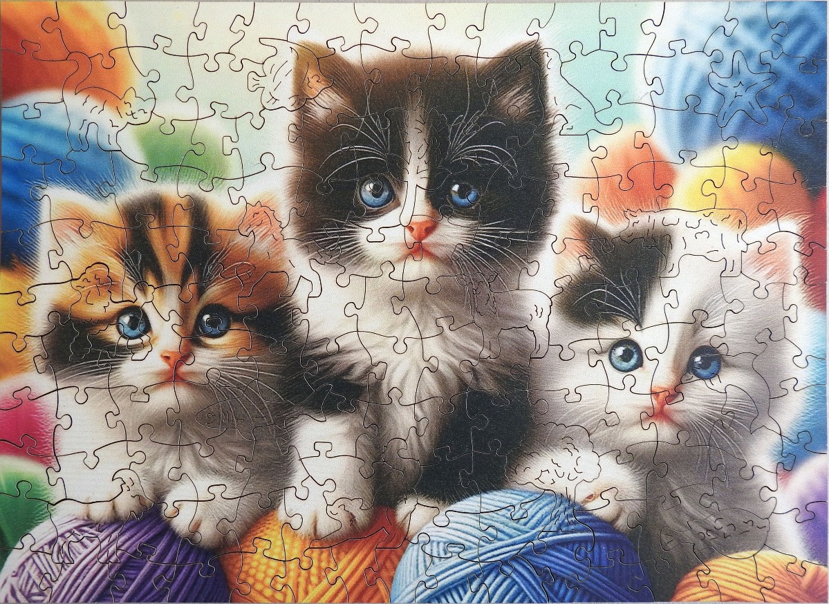 Three fluffy kittens with bright blue eyes sitting among colorful balls of yarn.