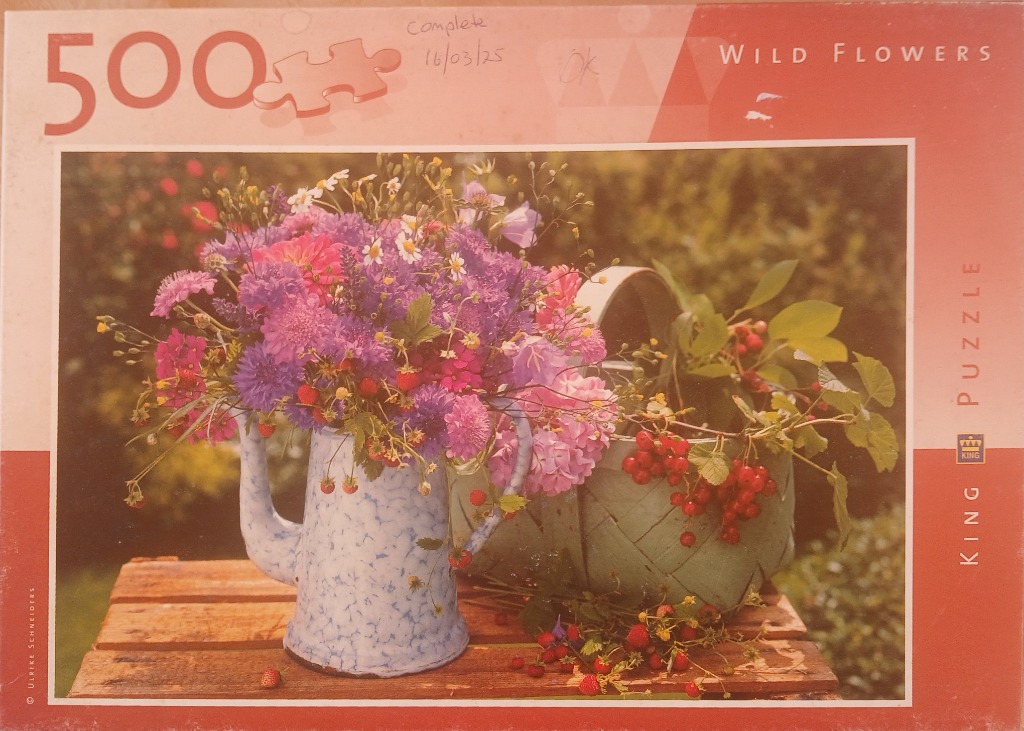 A bouquet of wild flowers in a speckled blue pitcher next to a small wooden basket filled with red berries.