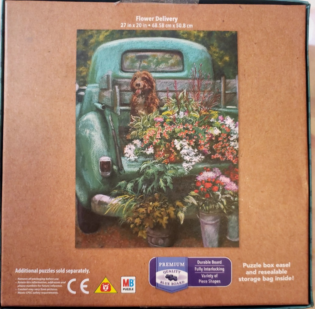A shaggy brown dog sits in the bed of a teal vintage pickup truck filled with colorful flowers.