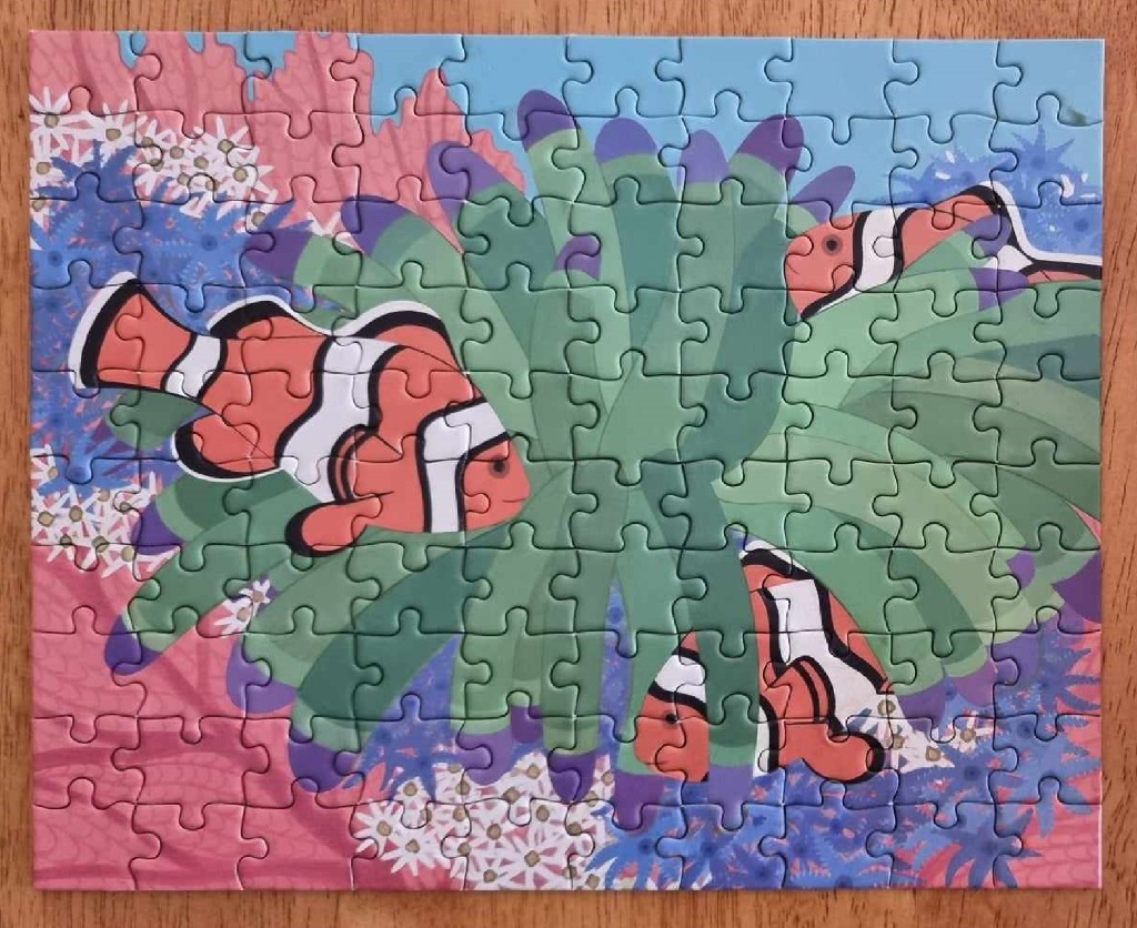 Illustration of three clownfish swimming among green sea anemones and coral reefs.