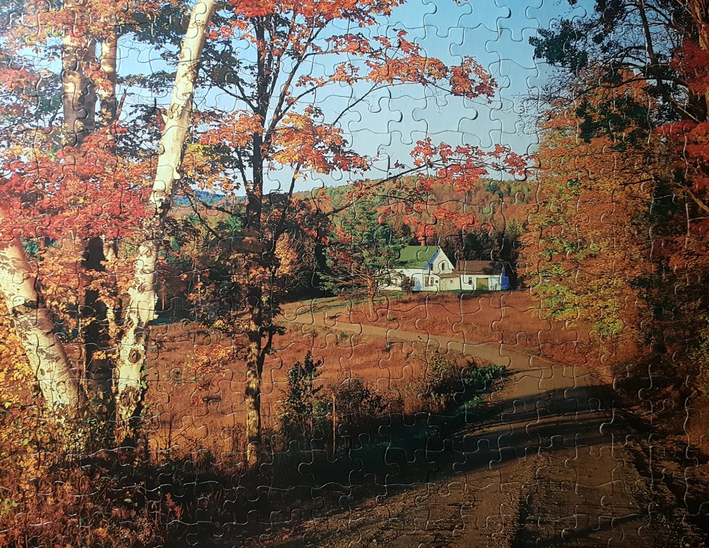 A peaceful autumn landscape featuring a white farmhouse nestled in a golden field framed by colourful trees.