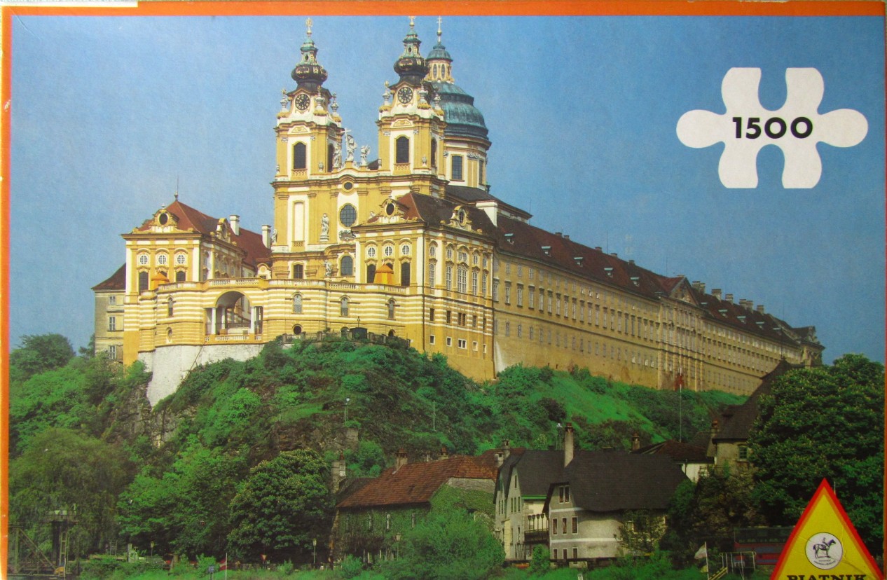 The baroque Melk Abbey in Austria perched on a rocky cliff above a town, shown in a clear daytime photograph.