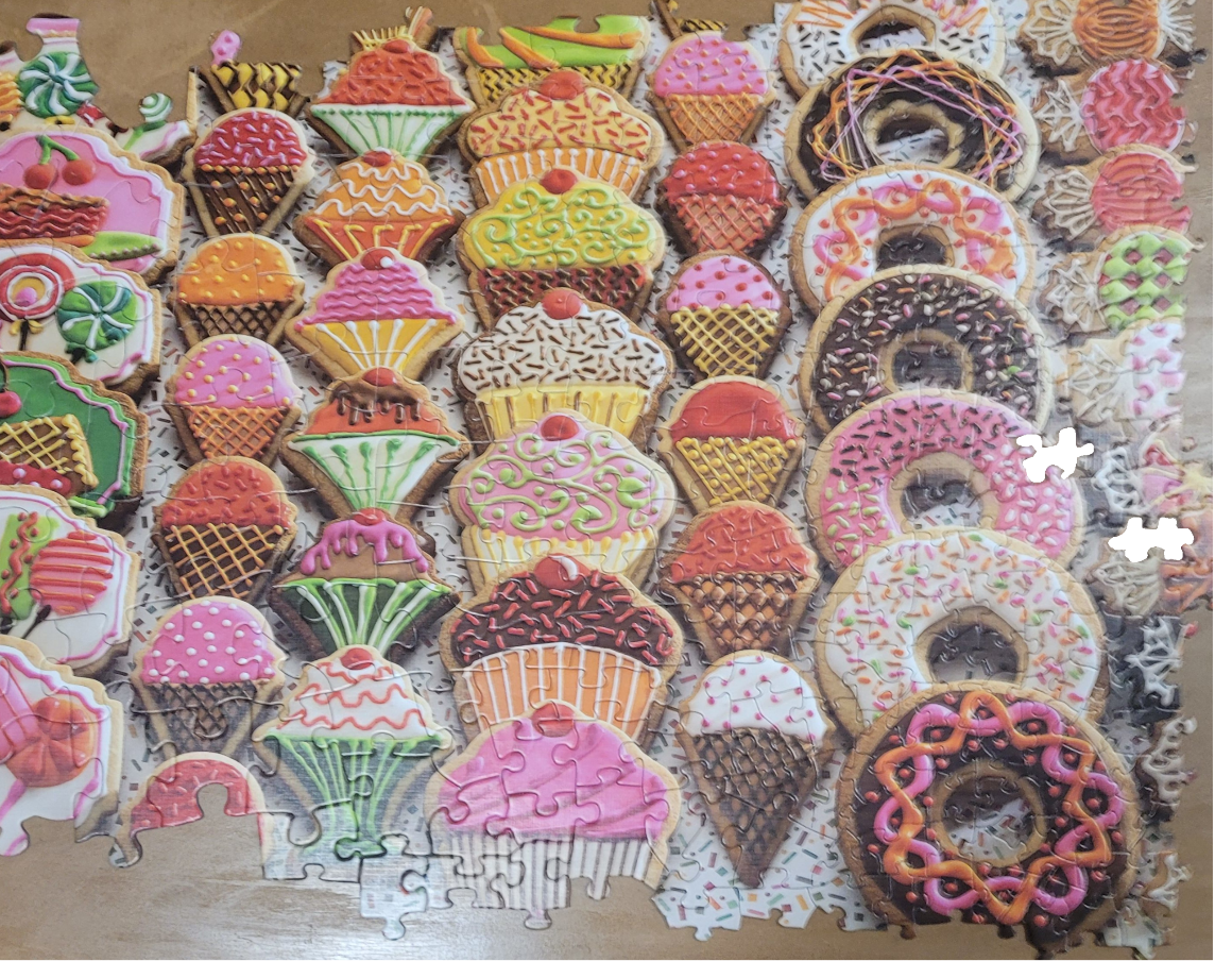 An assortment of colorful decorated sugar cookies shaped like ice cream cones, cupcakes, and donuts.