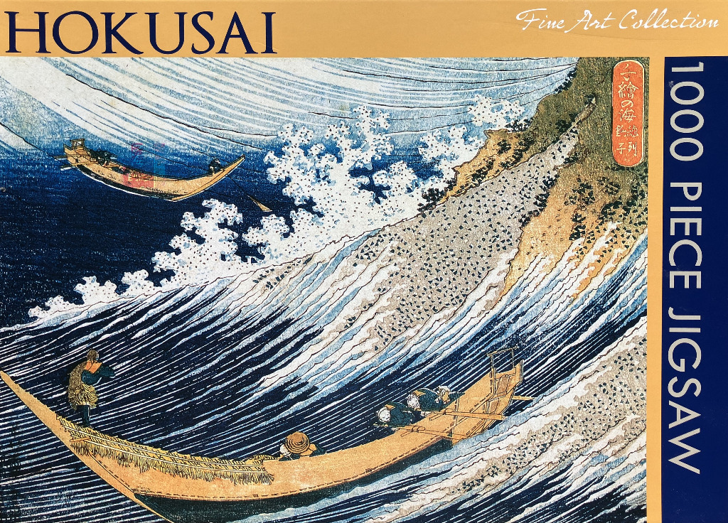 A woodblock print by Hokusai depicting boats tossed on choppy waves near a rocky, sandy shoreline.