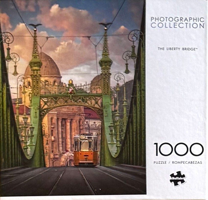 A vintage yellow tram travels across the green Liberty Bridge in Budapest towards a grand building with a large dome.