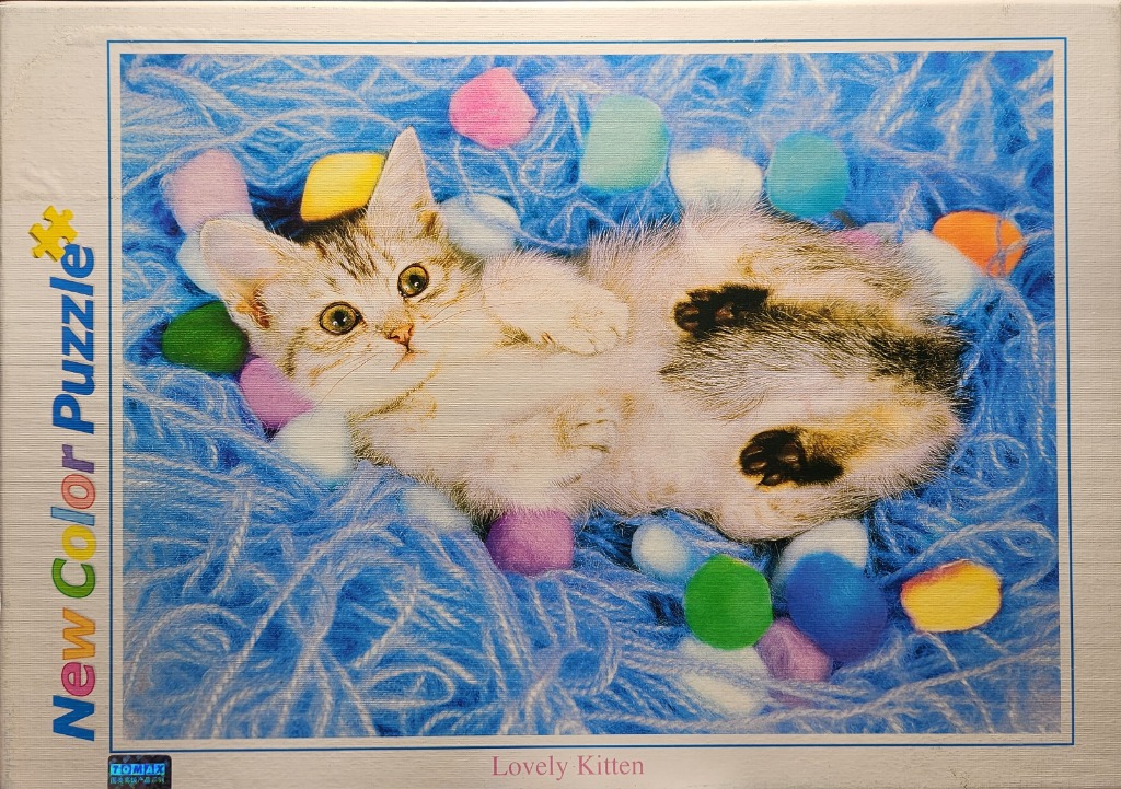 A fluffy tabby kitten lying on its back in a nest of bright blue yarn balls