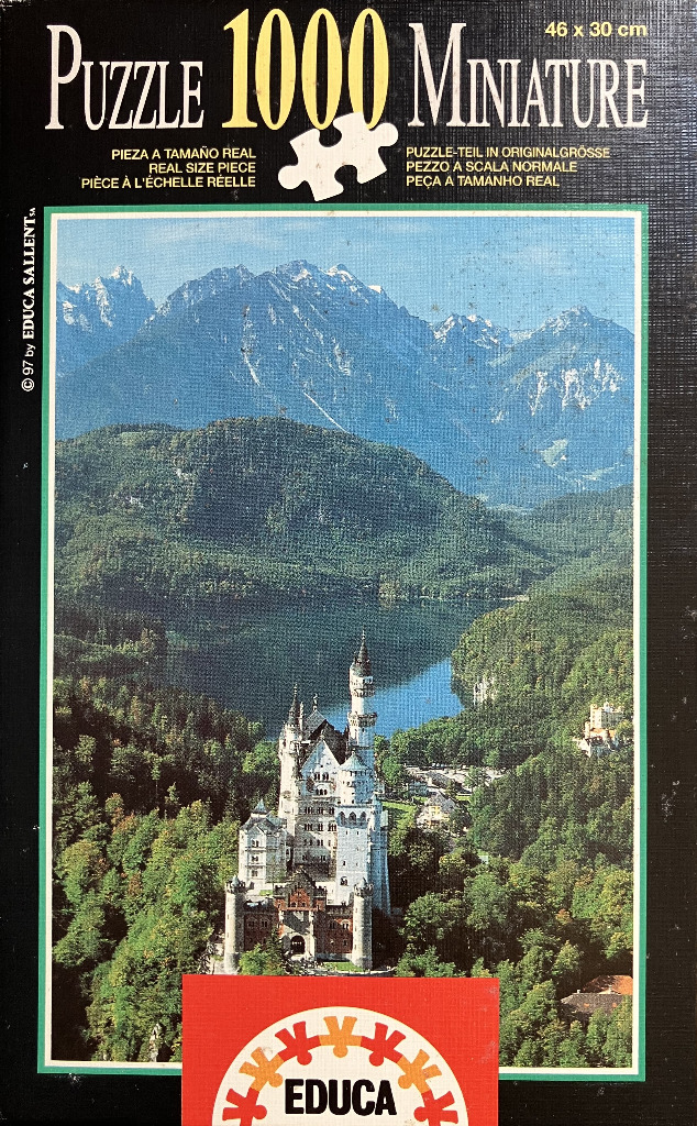 Neuschwanstein Castle nestled in a lush green valley before towering snow-capped mountain peaks.