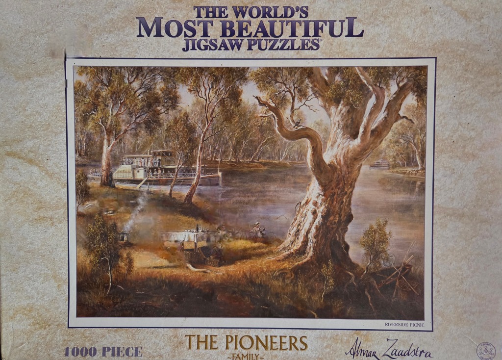 A scenic oil painting of an old paddle steamer boat docked by a riverbank with a picnic scene in the foreground.