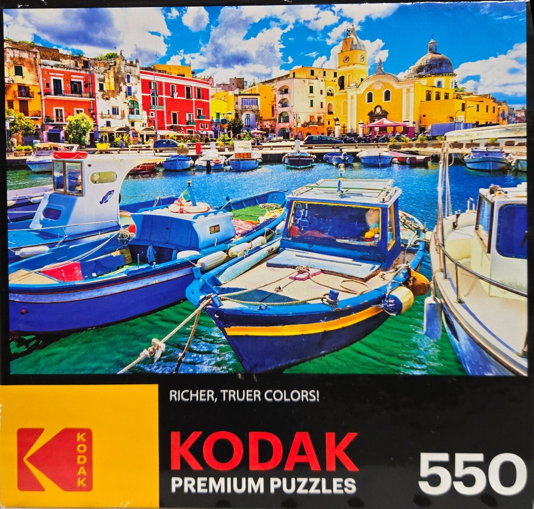 A sunny waterfront scene in an Italian coastal town with blue fishing boats moored in a harbor before colorful buildings.