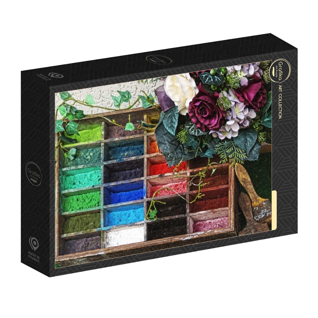 A wooden printer's tray filled with colorful powdered pigments, adorned with floral arrangements and a paintbrush.