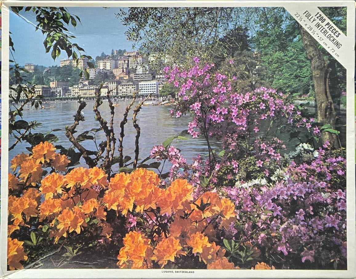 View of Lugano, Switzerland featuring vibrant orange and pink azalea bushes in the foreground and a lake in the back.
