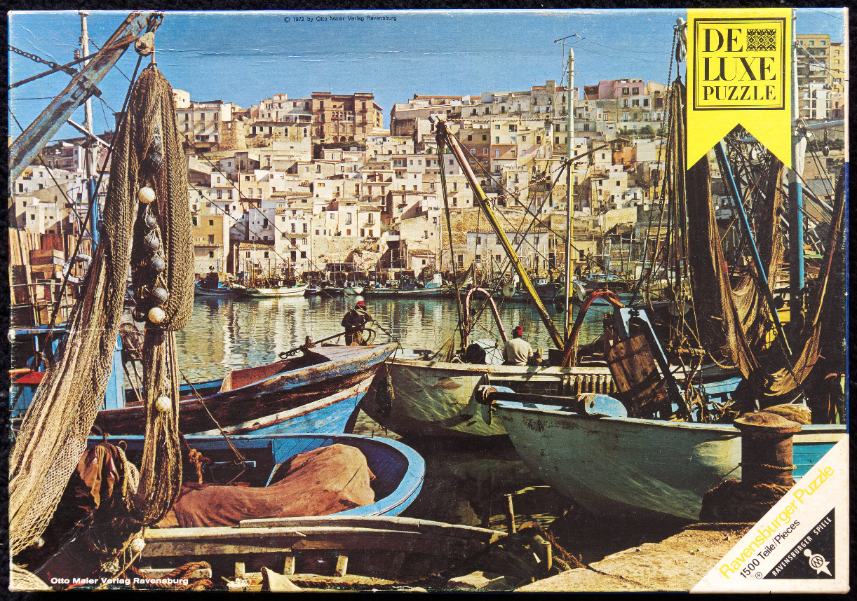 A Mediterranean harbor scene featuring wooden fishing boats, stacked white buildings on a hillside, and hanging nets.