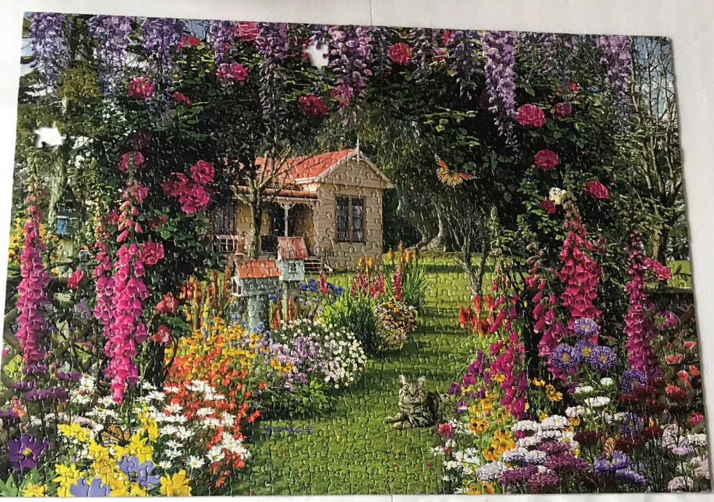 A cozy cottage surrounded by vibrant spring flowers and a cat in a lush garden.