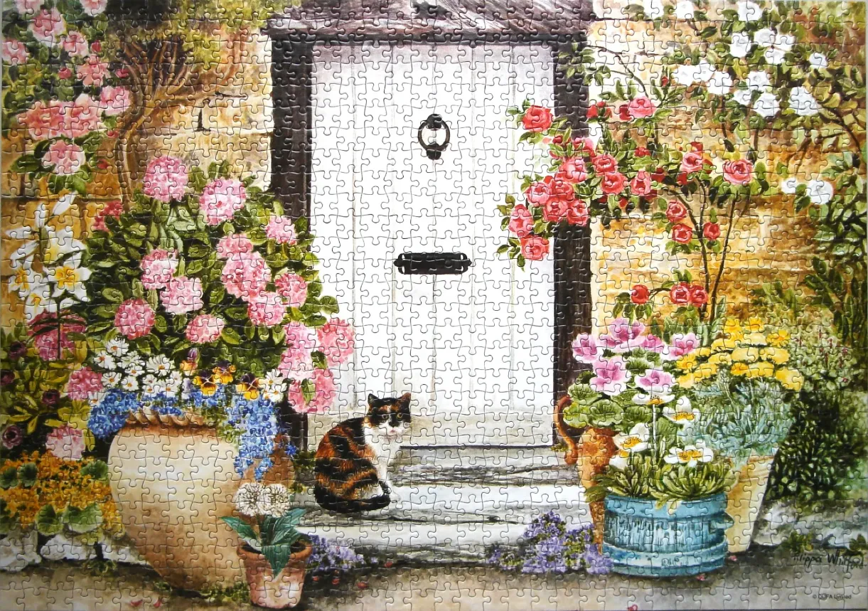 A calico cat sitting on stone steps in front of a white wooden door surrounded by lush potted flowers.