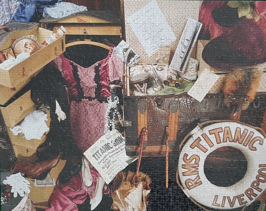 Victorian era items and "RMS Titanic" life preserver, featuring pink dress & vintage luggage.