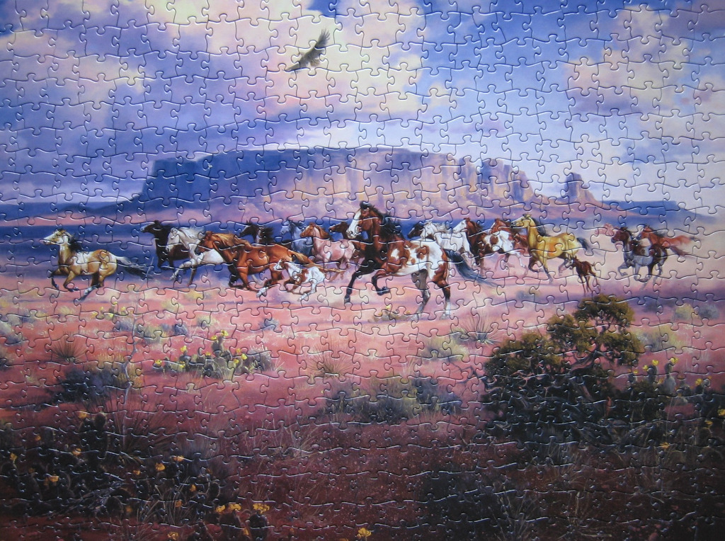 A herd of horses running across a desert landscape beneath a dramatic sunset sky.