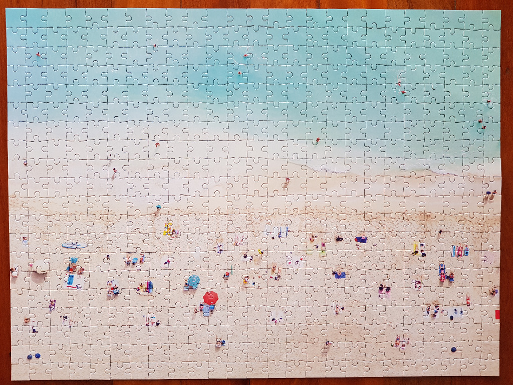 Aerial view of a sunny beach with swimmers in turquoise water and colorful umbrellas on the sand.