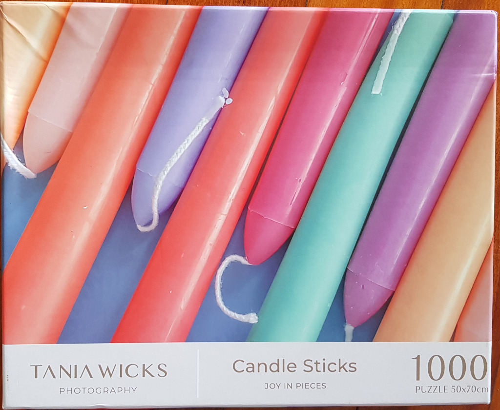 A diagonal arrangement of colorful taper candles in shades of orange, purple, pink, and teal against a blue background.