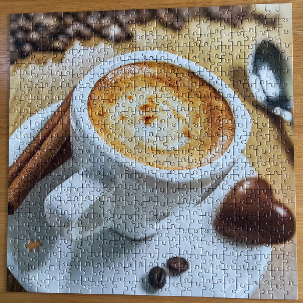 A close-up photograph of a cup of coffee with cinnamon sticks and a heart-shaped chocolate.
