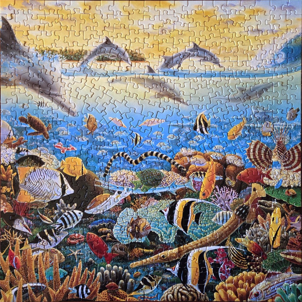 An underwater reef scene with coral, colorful tropical fish, and dolphins jumping above the surface at sunset.