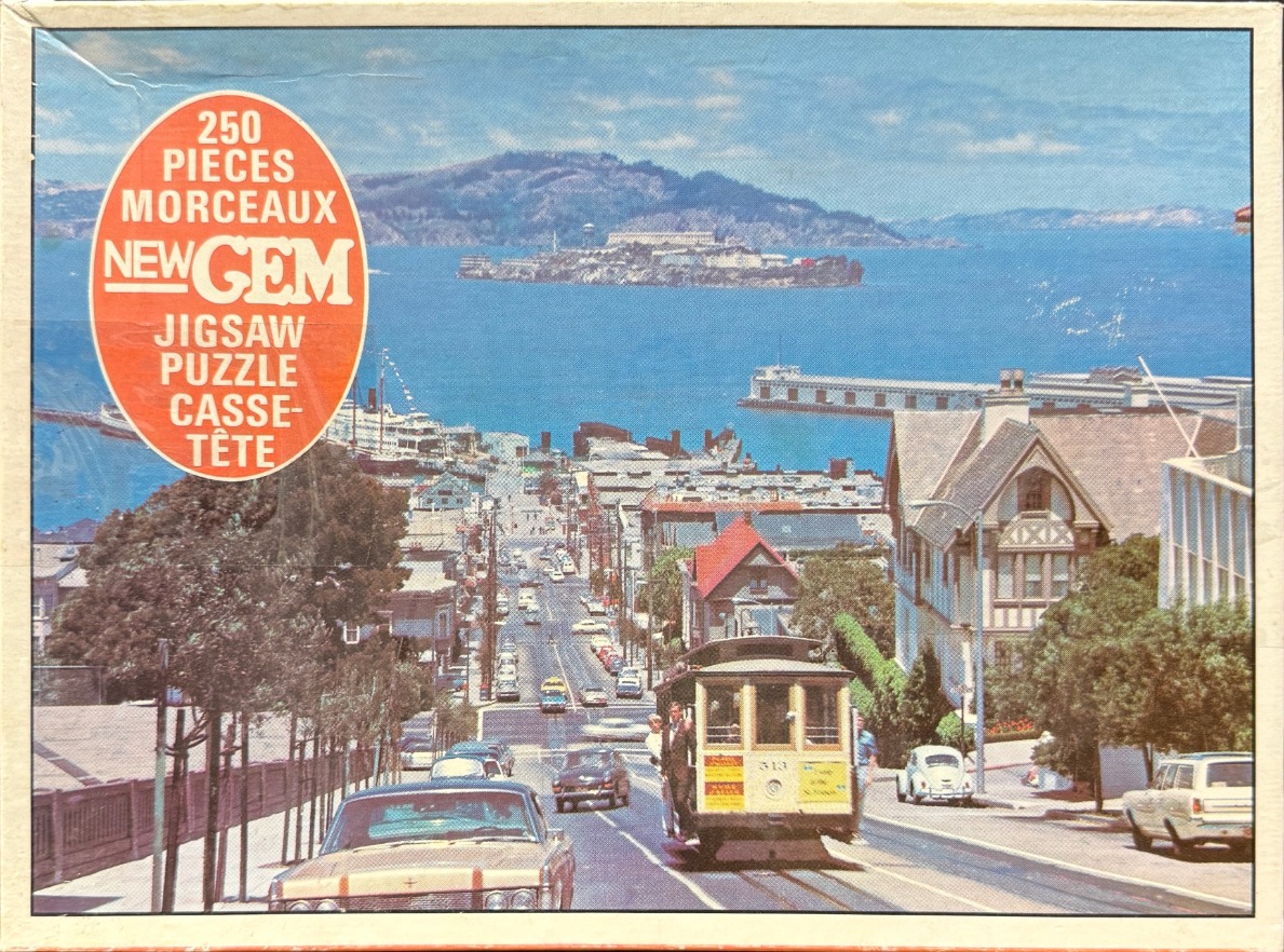 A vintage photograph of a San Francisco cable car traveling down a steep street overlooking the bay and Alcatraz Island.