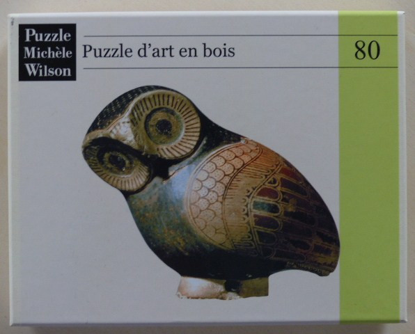 A close-up photograph of an ancient ceramic owl figurine, possibly Greek, set against a white background.