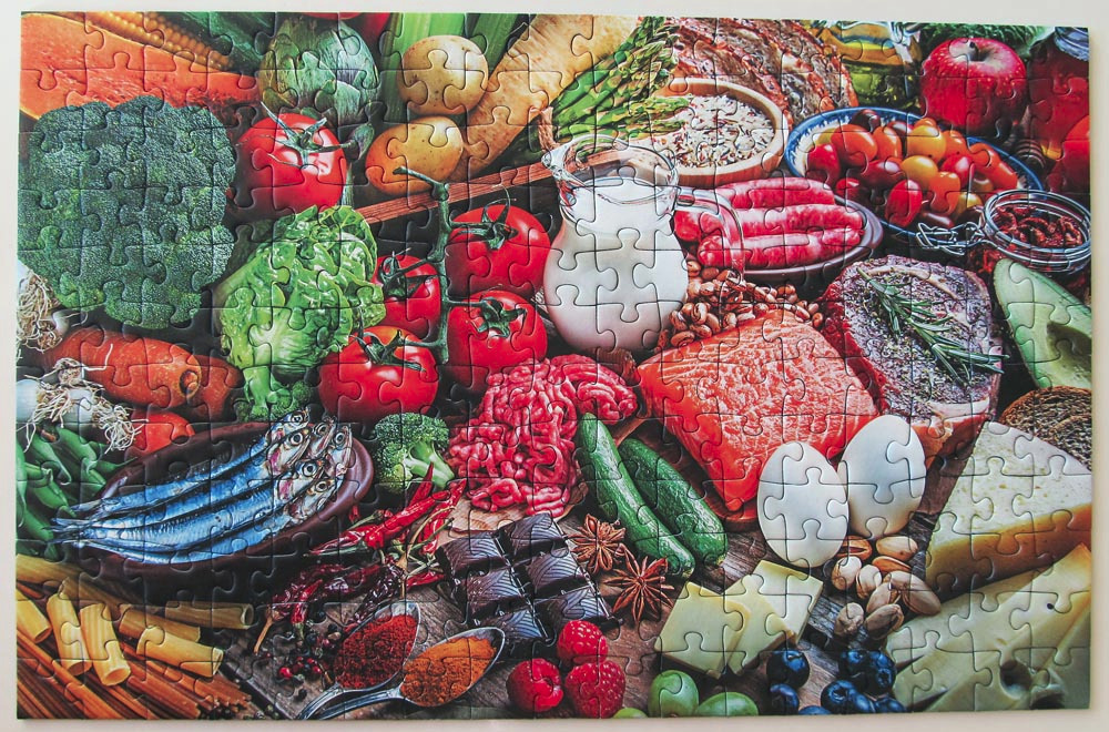 A high-angle, crowded food table display featuring various fresh ingredients including vegetables, meat, fish, and dairy.