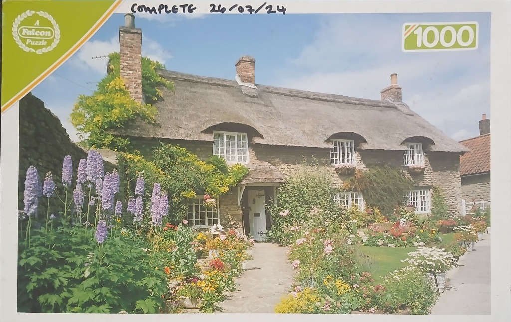 A thatched stone cottage surrounded by a vibrant flower garden on a sunny day.