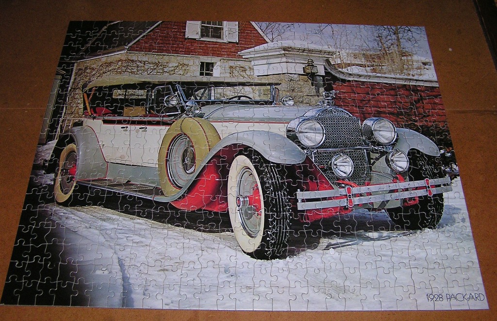 A vintage 1928 Packard automobile parked in the snow in front of a brick building.