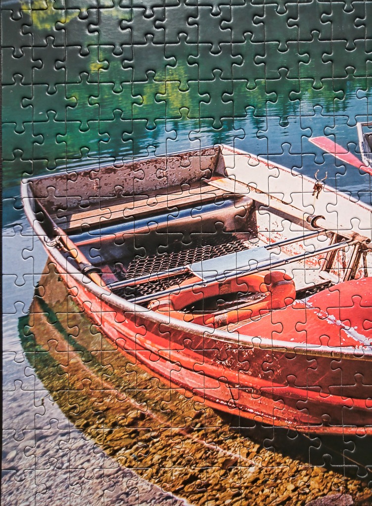 A weathered red rowboat moored on a calm lake with a pebbled shoreline.