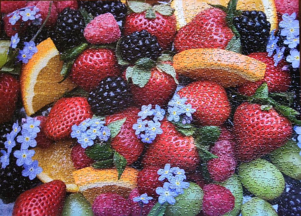 A close-up, top-down view of a colorful assortment of fresh strawberries, blackberries, raspberries, orange slices, and small