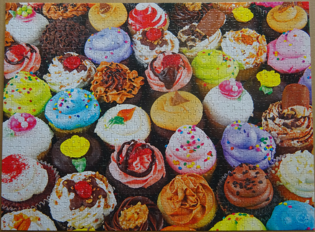 A vibrant, high-angle display of many different decorated cupcakes with frosting and toppings.