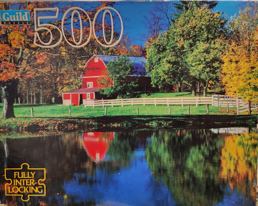 A traditional red barn surrounded by autumn trees reflected in a calm pond.