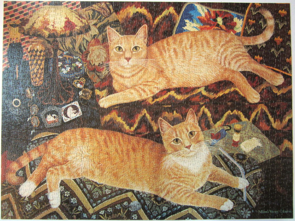 Two ginger cats resting in a room with patterned textiles and various objects.