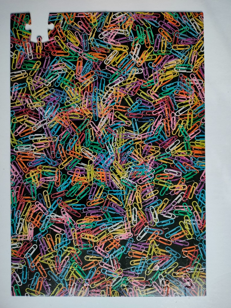 A dense pattern of colorful vinyl-coated paperclips scattered against a solid black background.